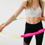crop sportswoman exercising with gymnastic hula hoop